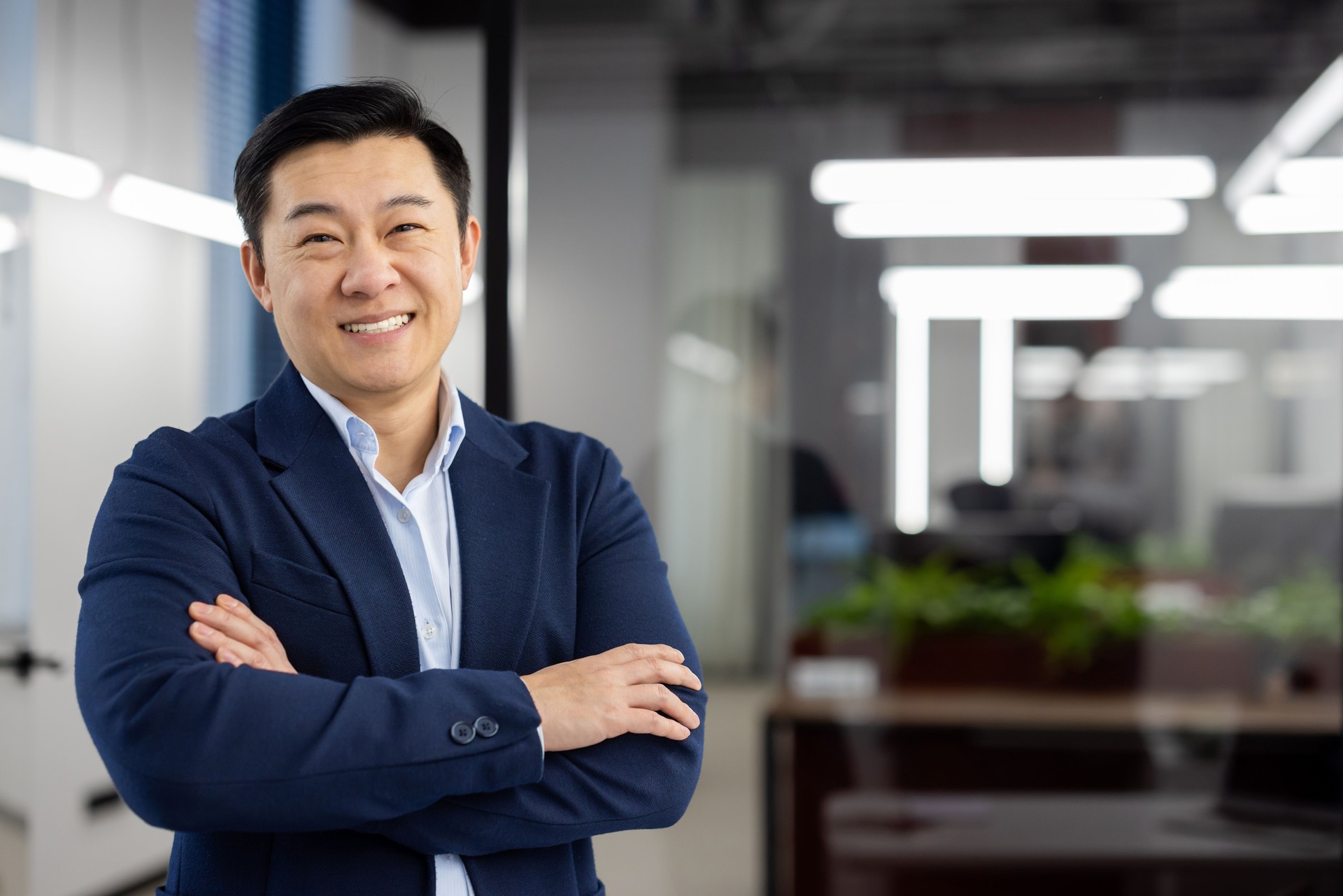 Portrait of successful asian businessman inside office at workplace, man in business suit smiling looking at camera, mature boss with crossed arms, successful financier broker