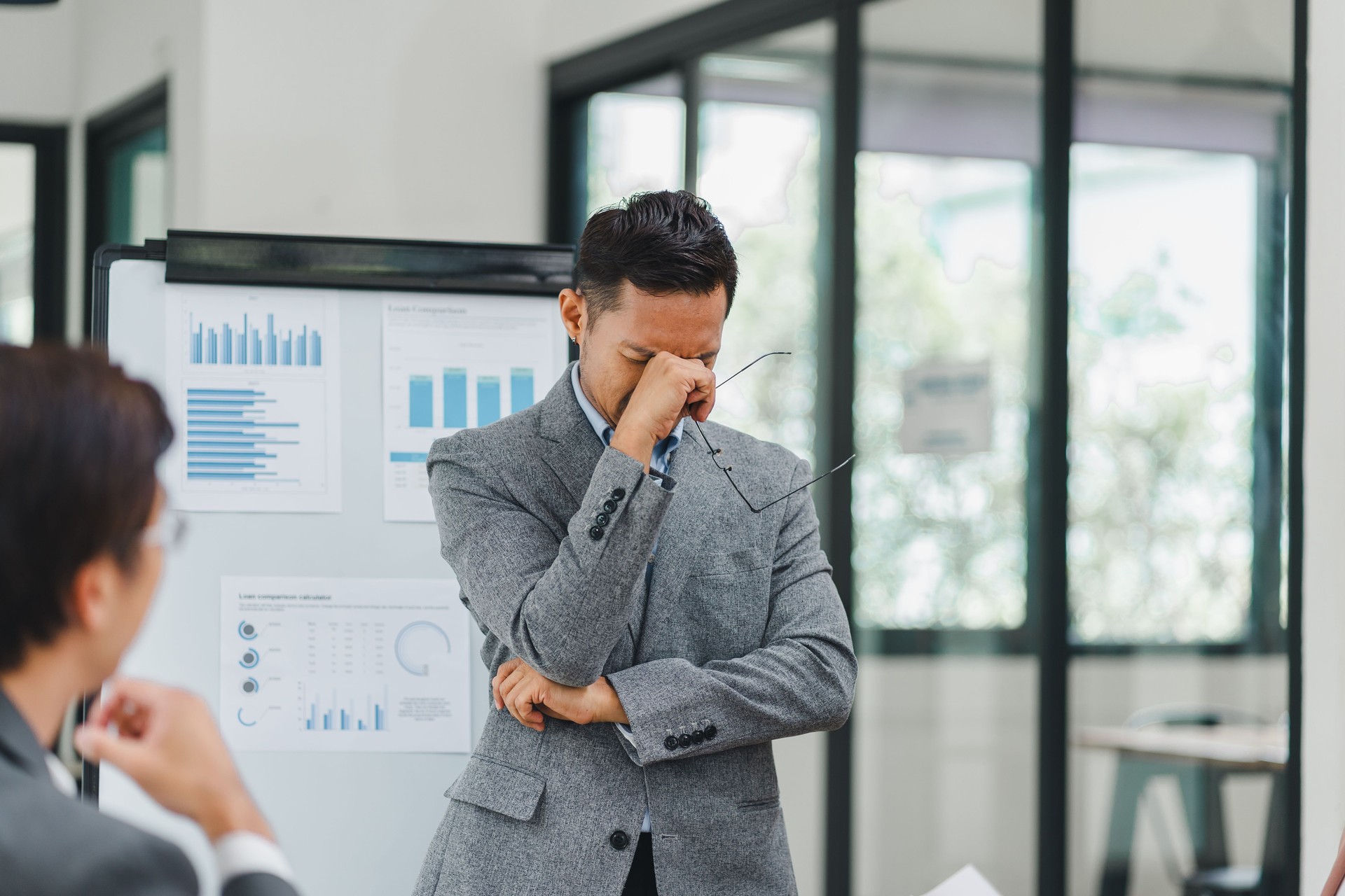 Pensive businessman deep in thought while presenting data charts and graphs during a meeting with colleagues in a modern office.